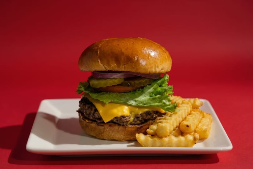 Cheeseburger with lettuce, tomato, onion, and pickles, served with crinkle-cut fries on a white plate.